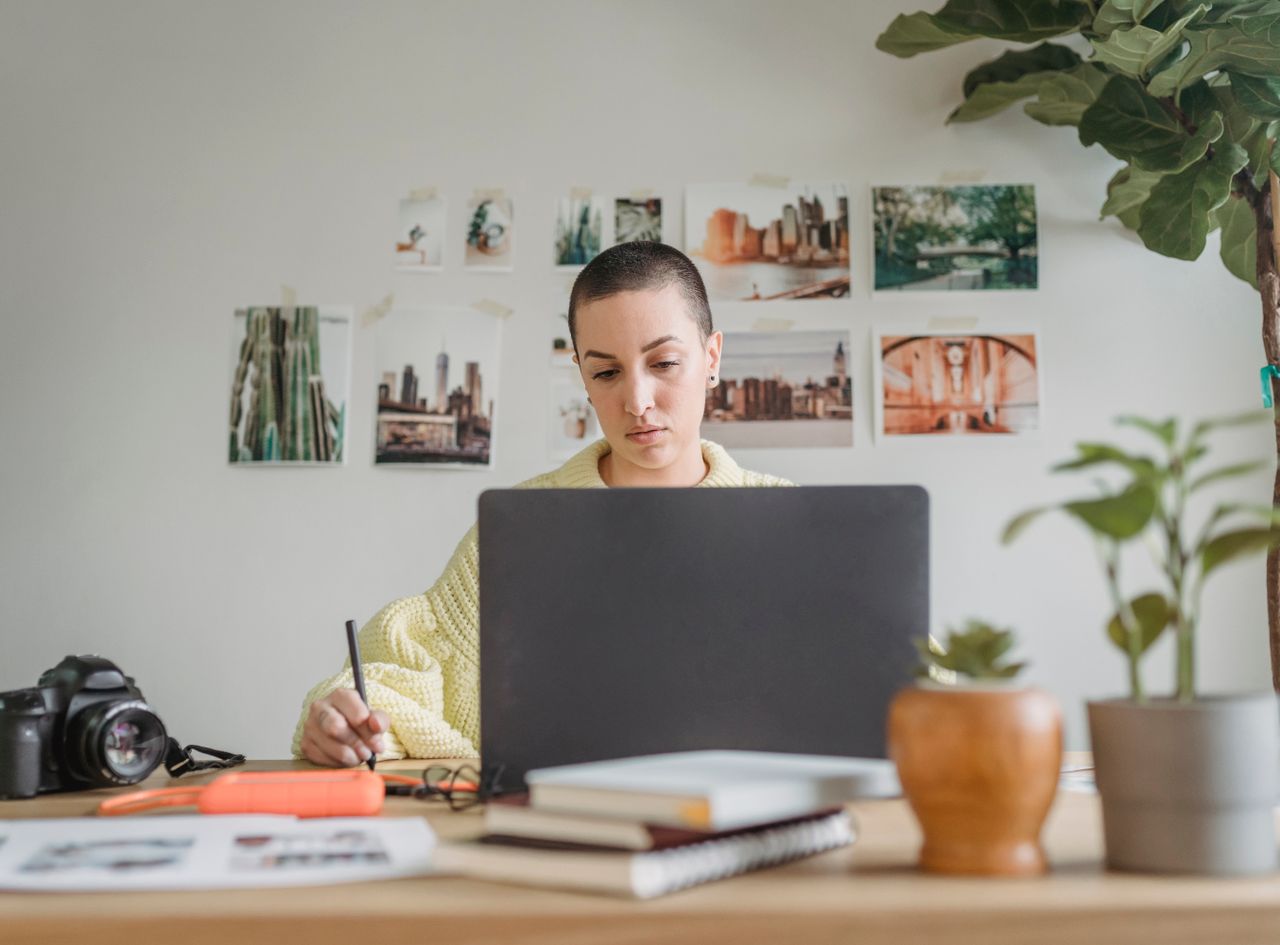 About Professional female designer looking at laptop and using graphic tablet while sitting at table in light workspace