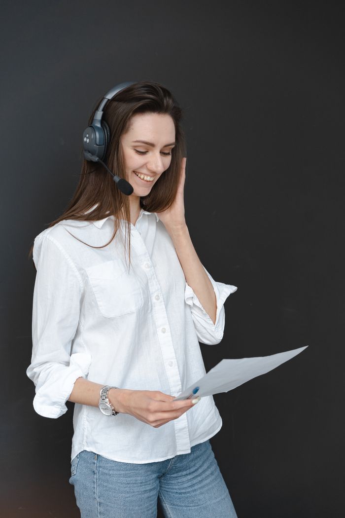 A smiling woman in a headset providing customer service, holding paper.