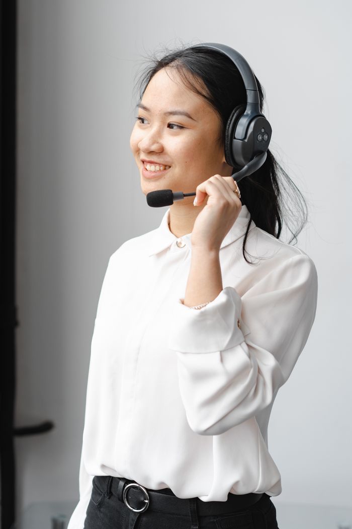 About Smiling Asian woman with headset providing customer support in an office setting.