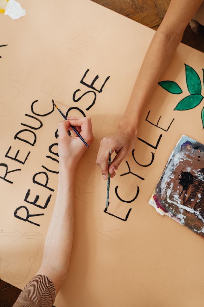 Close-up of hands painting Reduce, Recycle, Repurpose slogan on canvas.